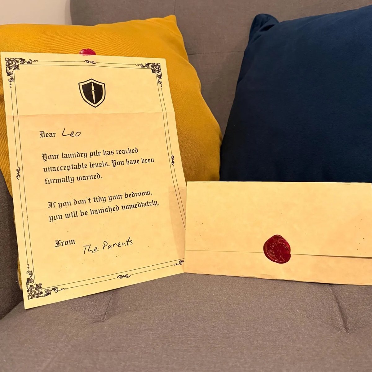 A finished decree on yellowed parchment beside its envelope, pressed with a crimson wax seal